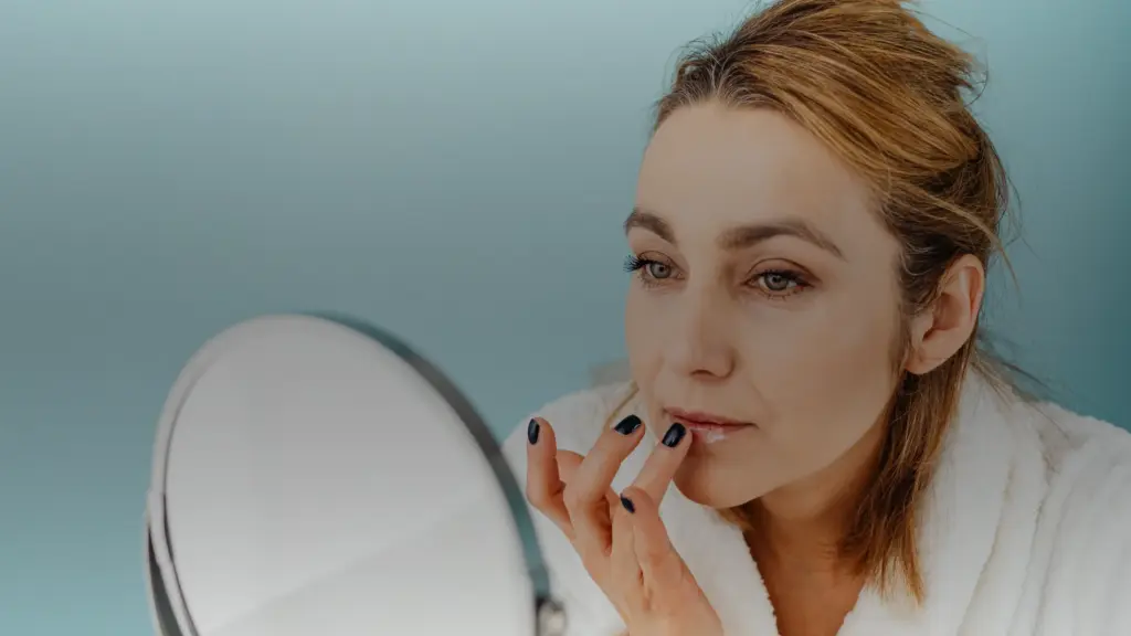 Une femme applique un soin sur ses lèvres devant un miroir
